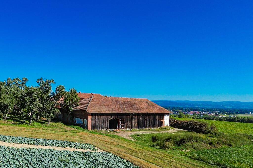 Weitläufige Ansicht eines alten Bauernhofs mit Feldern und einem Dorf in der Ferne unter blauem Himmel.