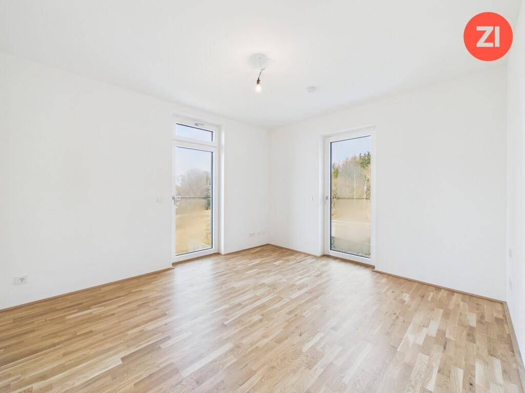 Heller Raum mit Holzboden und zwei großen Fenstern, die viel Tageslicht hereinlassen.