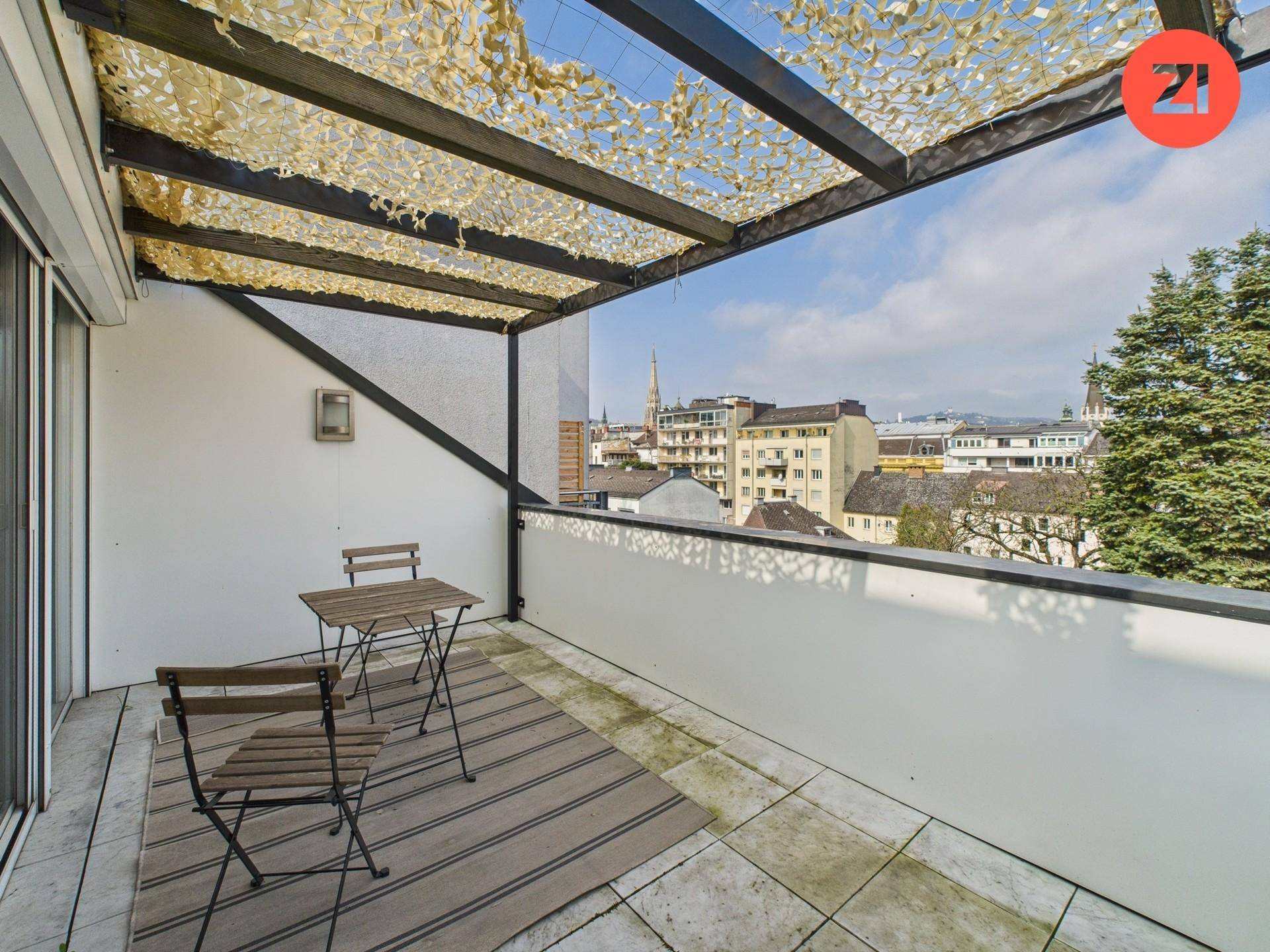 Geräumiger Balkon mit Sitzgelegenheiten und weitem Blick über die Stadt und umliegende Gebäude.