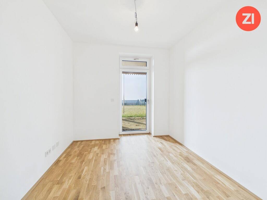 Lichtdurchflutetes Zimmer mit Holzboden und Blick ins Grüne.
