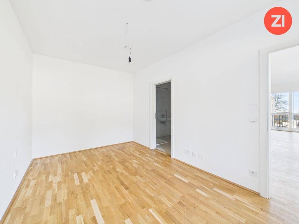 Leeres Schlafzimmer mit Holzboden und Zugang zu einem Badezimmer, hell und geräumig.