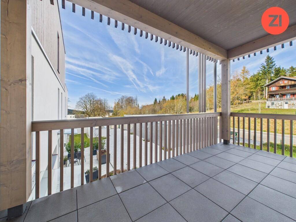 Geräumiger Balkon mit Holzelementen und Fliesenboden, bietet einen weiten Blick ins Grüne.