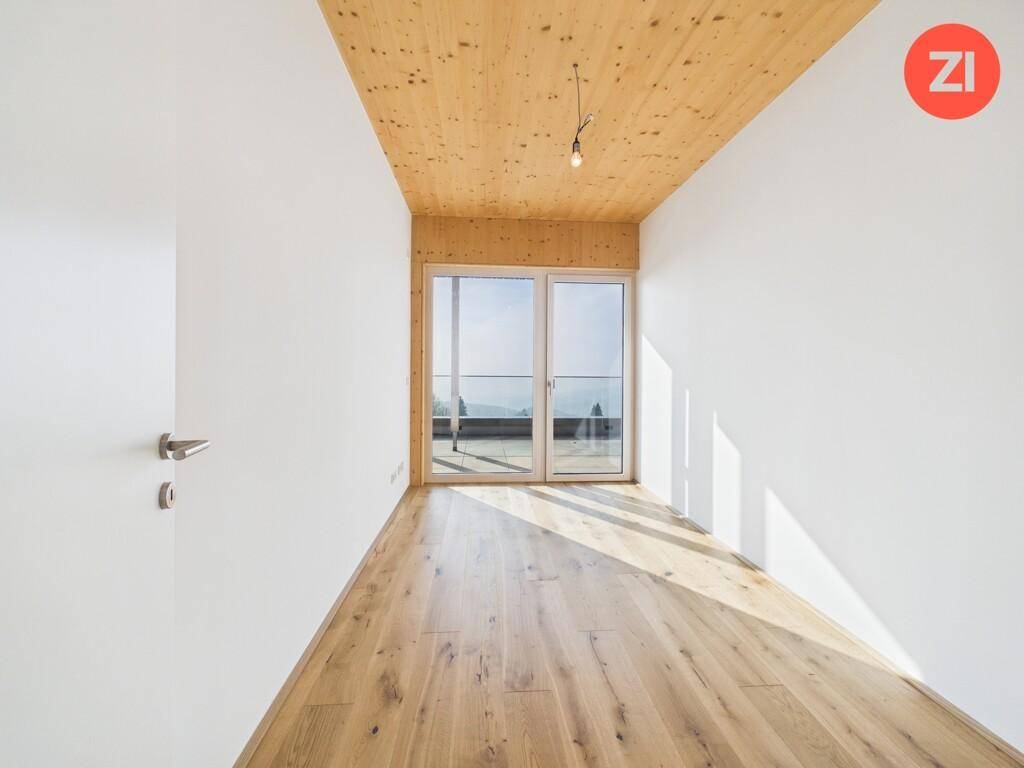 Lichtdurchflutetes Zimmer mit Holzboden, Holzdecke und großen Fenstern mit Weitblick.