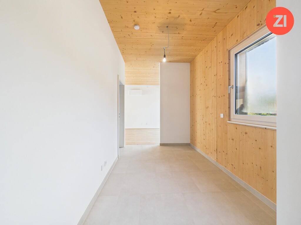 Heller Flur mit Holzboden, Holzdecke und einem Fenster, das Tageslicht hereinlässt.