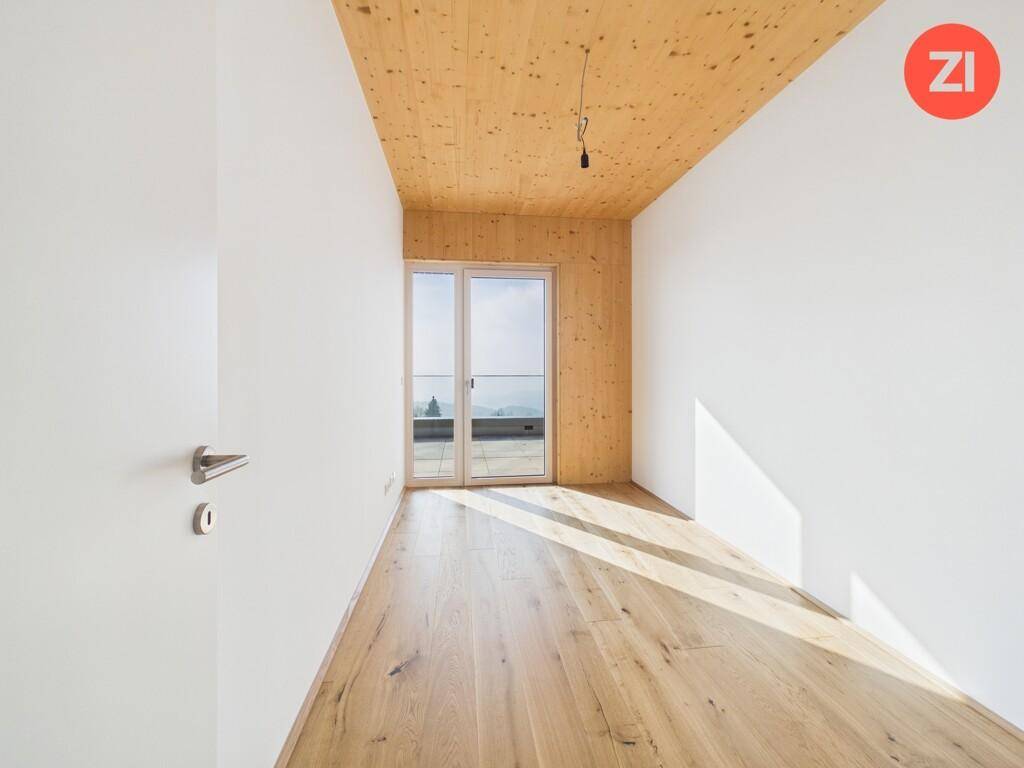 Sonniger Raum mit Holzboden, Holzdecke und großen Fenstern, die viel Licht spenden.