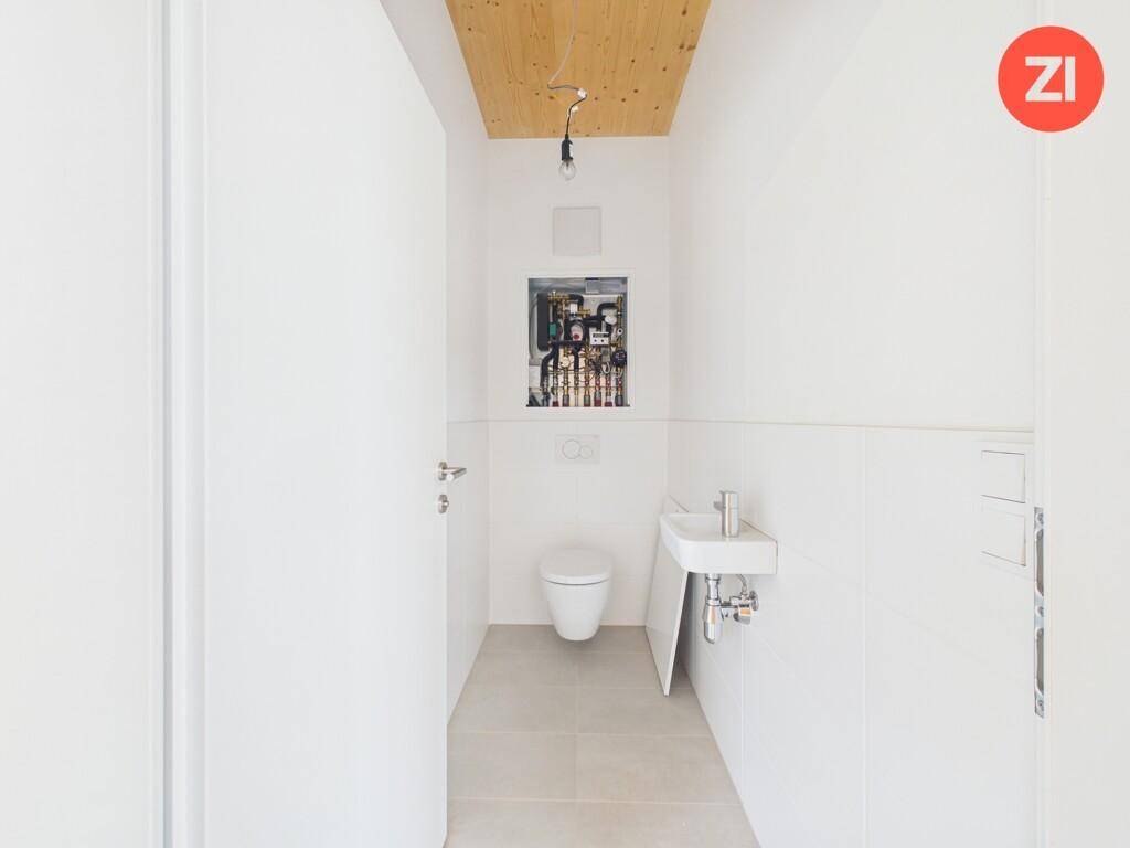 Gäste-WC mit wandhängender Toilette, kleinem Waschbecken und Fliesenboden.