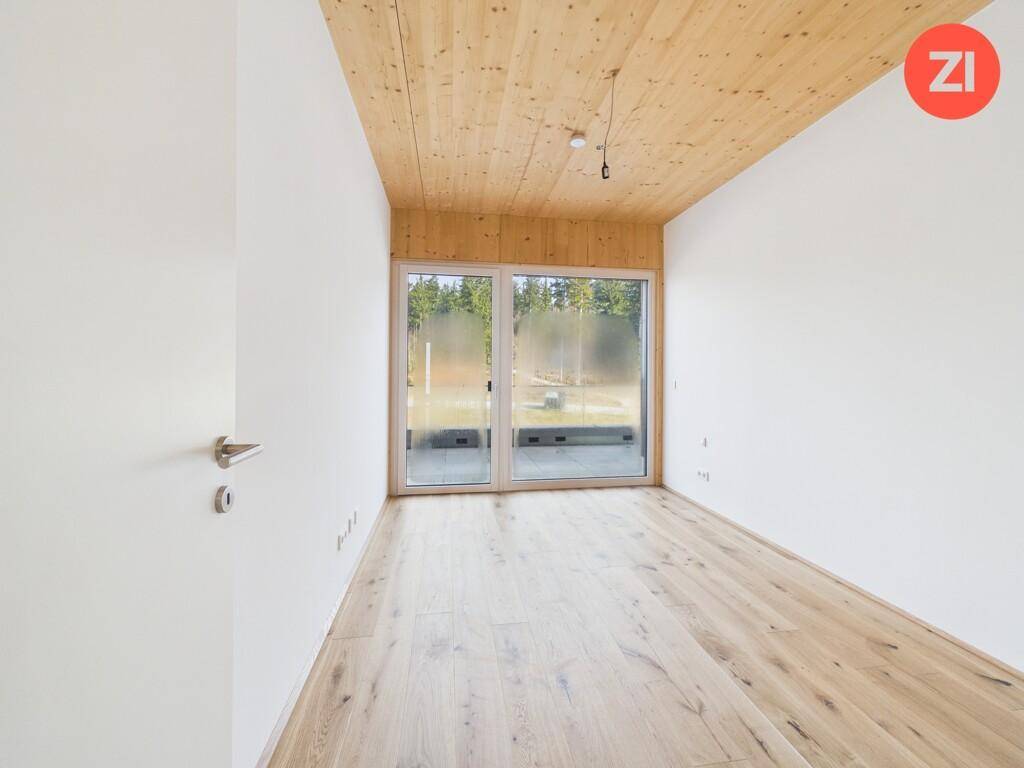 Helles Zimmer mit Holzboden, Holzdecke und großen Fenstern mit Blick ins Grüne.