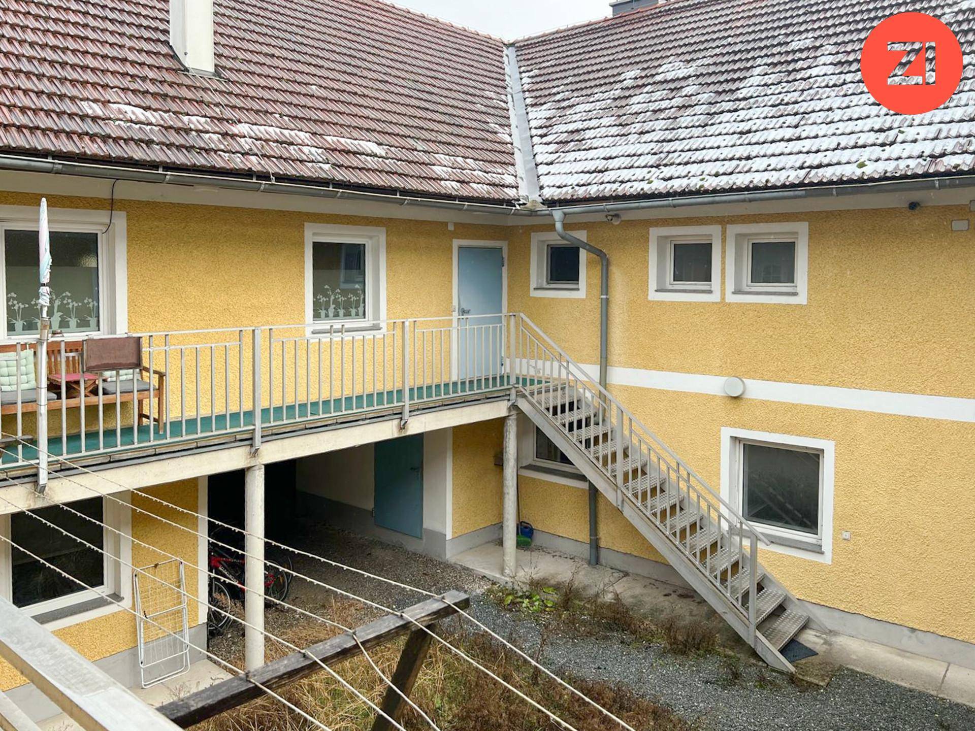 Innenhofbereich mit Außentreppe, die zu einem Balkon oder Laubengang im Obergeschoss führt.