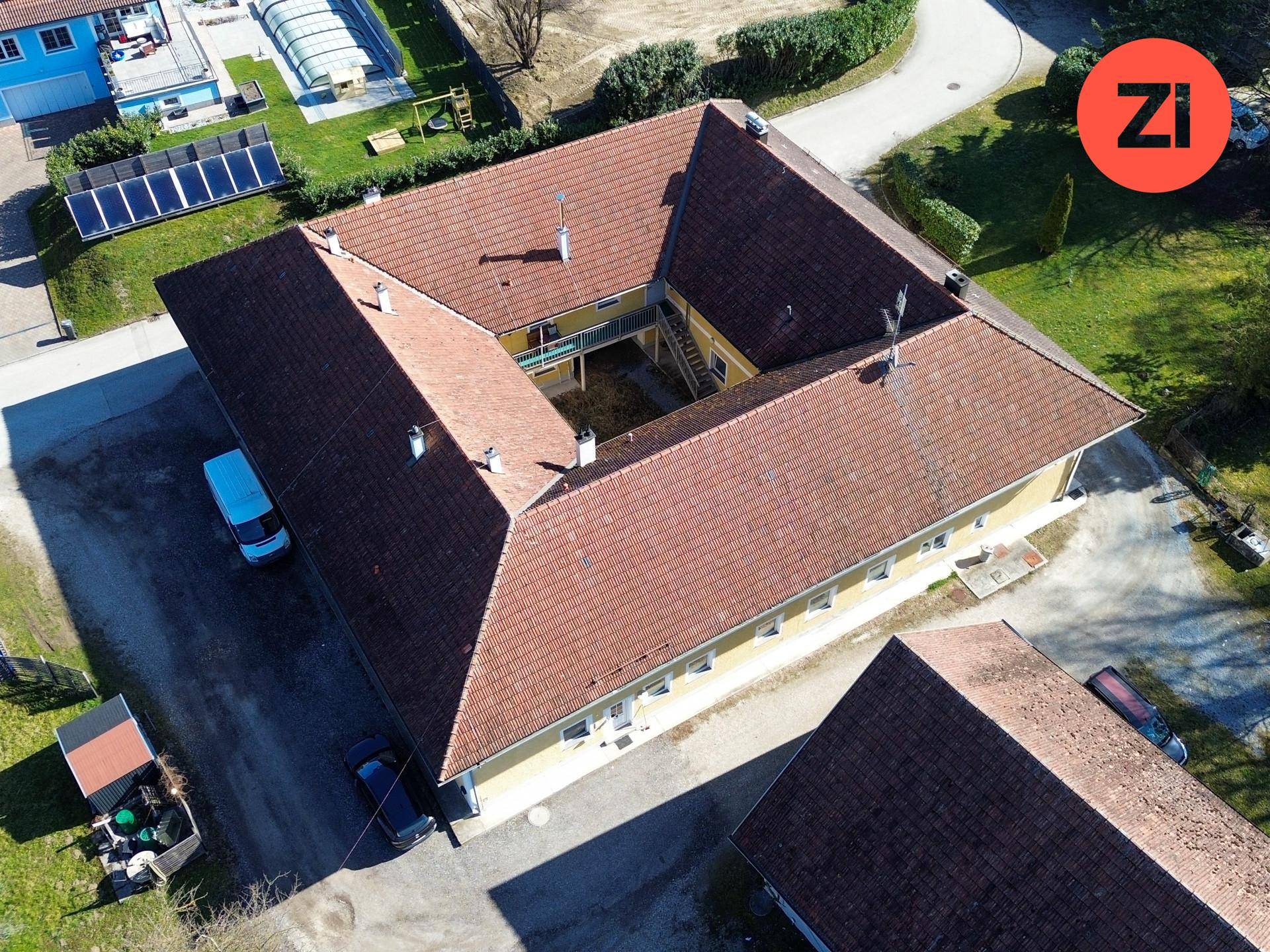 Luftaufnahme des U-förmigen Gebäudekomplexes und der Scheune, mit Solaranlagen in der Ferne.