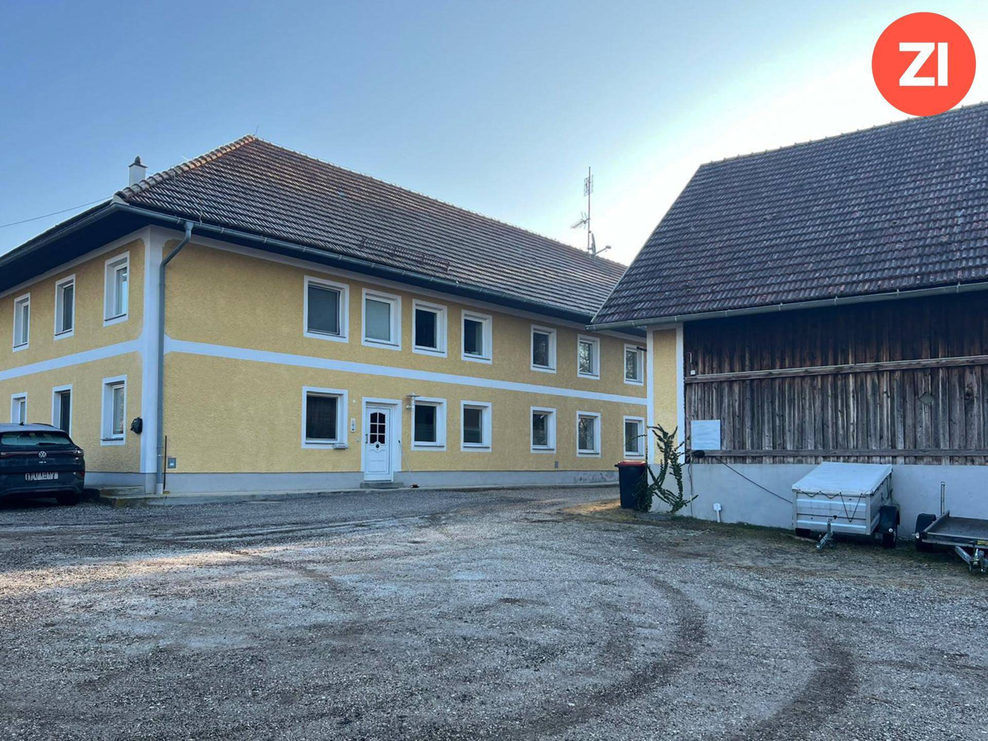 Außenansicht des Hauptgebäudes und der Scheune mit großem Schotterparkplatz im Vordergrund.