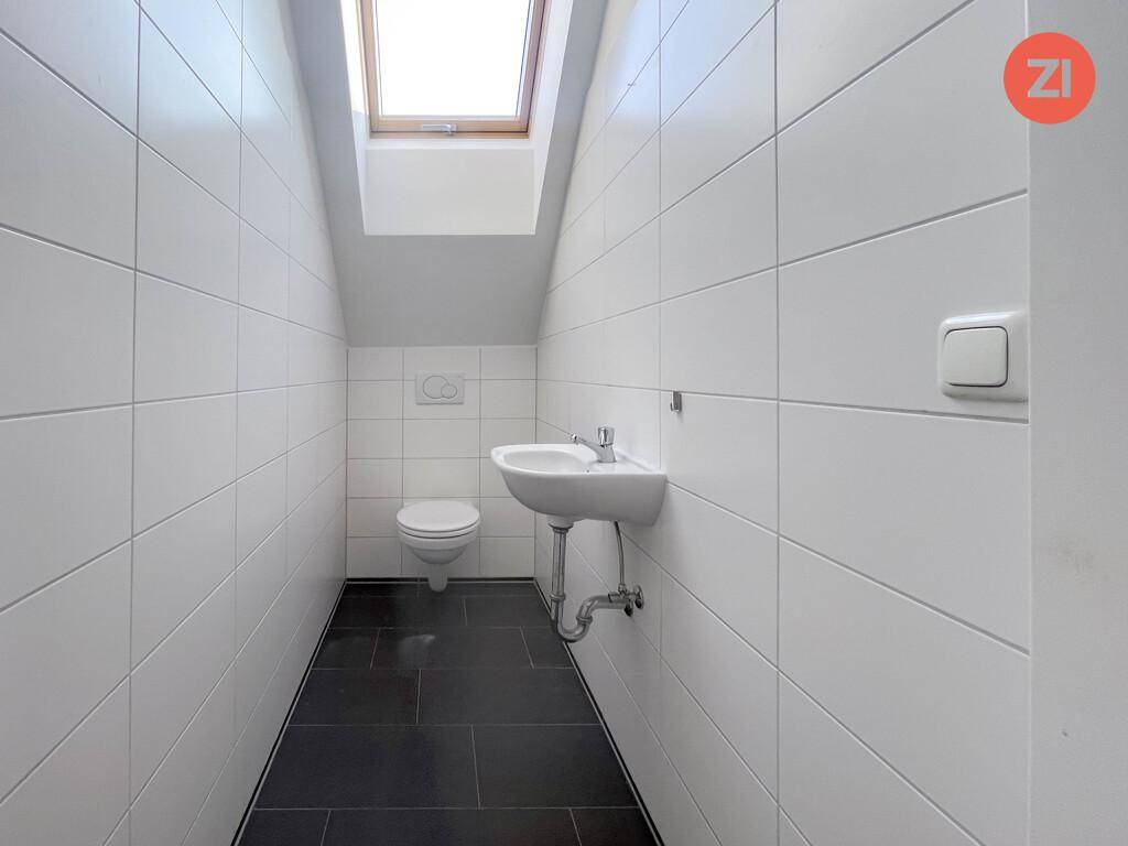 Kleines Gäste-WC mit weißen Fliesen, Waschbecken und Dachfenster für natürliche Belüftung.