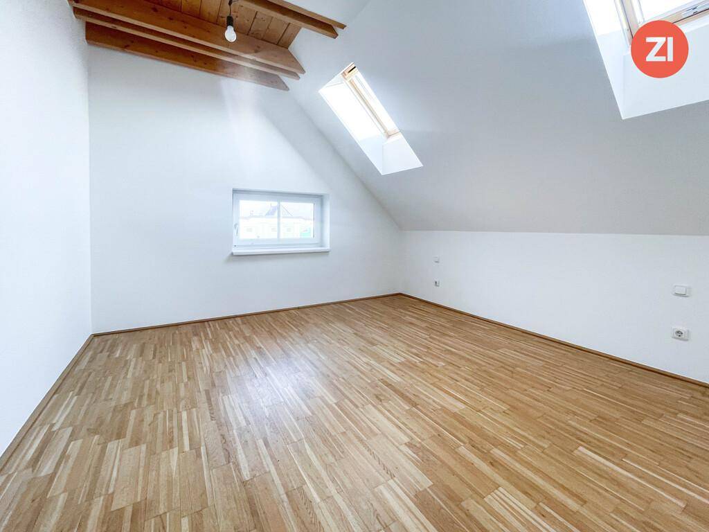 Gemütliches Zimmer im Dachgeschoss mit Holzboden, Dachfenster und einem weiteren Fenster für Tageslicht.