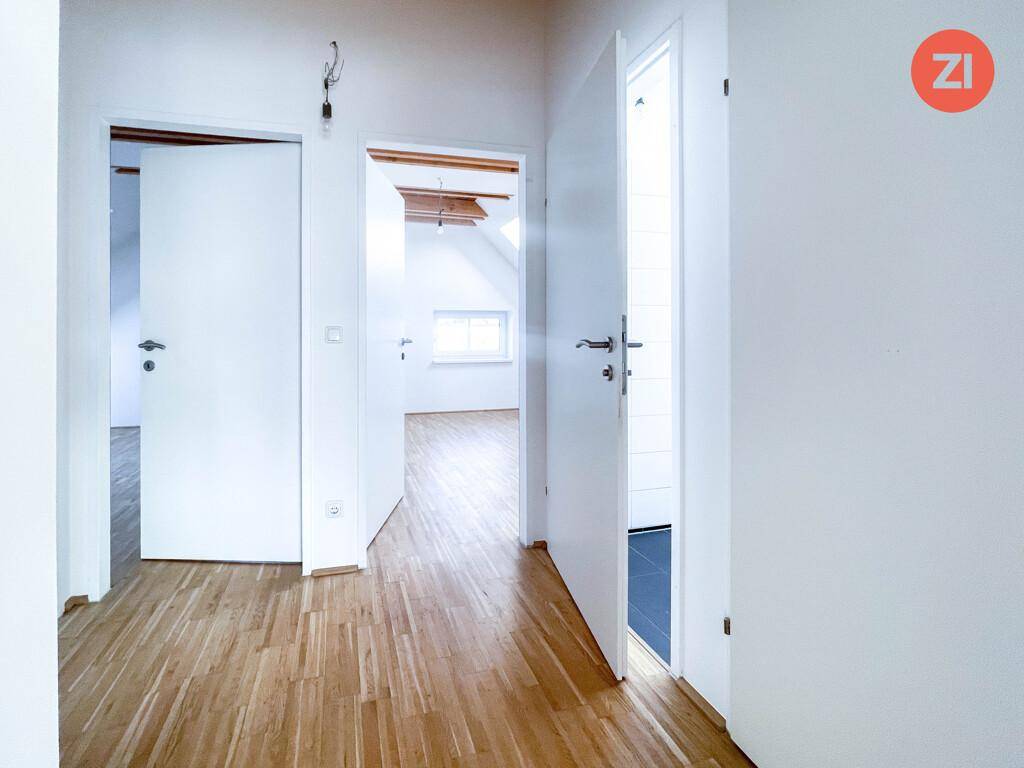 Heller Flur mit Holzboden und weißen Türen, der zu verschiedenen Räumen im Dachgeschoss führt.