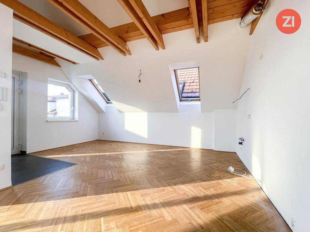 Heller Dachbodenraum mit Holzbalken, Parkettboden und mehreren Dachfenstern, die viel Licht spenden.