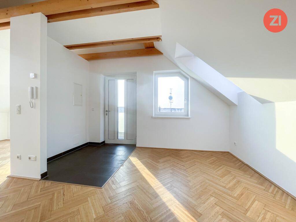 Lichtdurchfluteter Dachbodenraum mit Holzbalken, Parkettboden und einem Fenster, das Tageslicht hereinlässt.