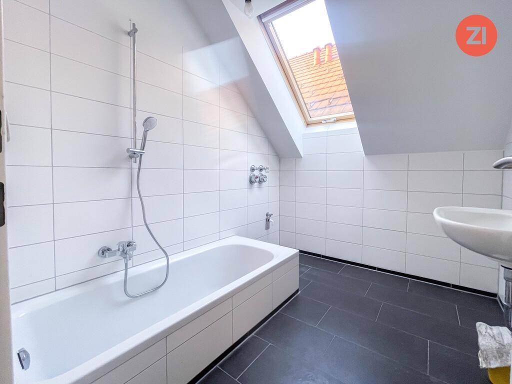 Modernes Badezimmer mit weißen Fliesen, Badewanne und Dachfenster, das für Helligkeit sorgt.
