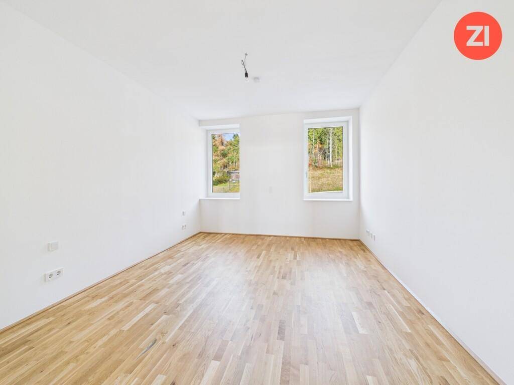 Geräumiges Zimmer mit zwei Fenstern, Parkettboden und Blick auf die umliegende Natur.