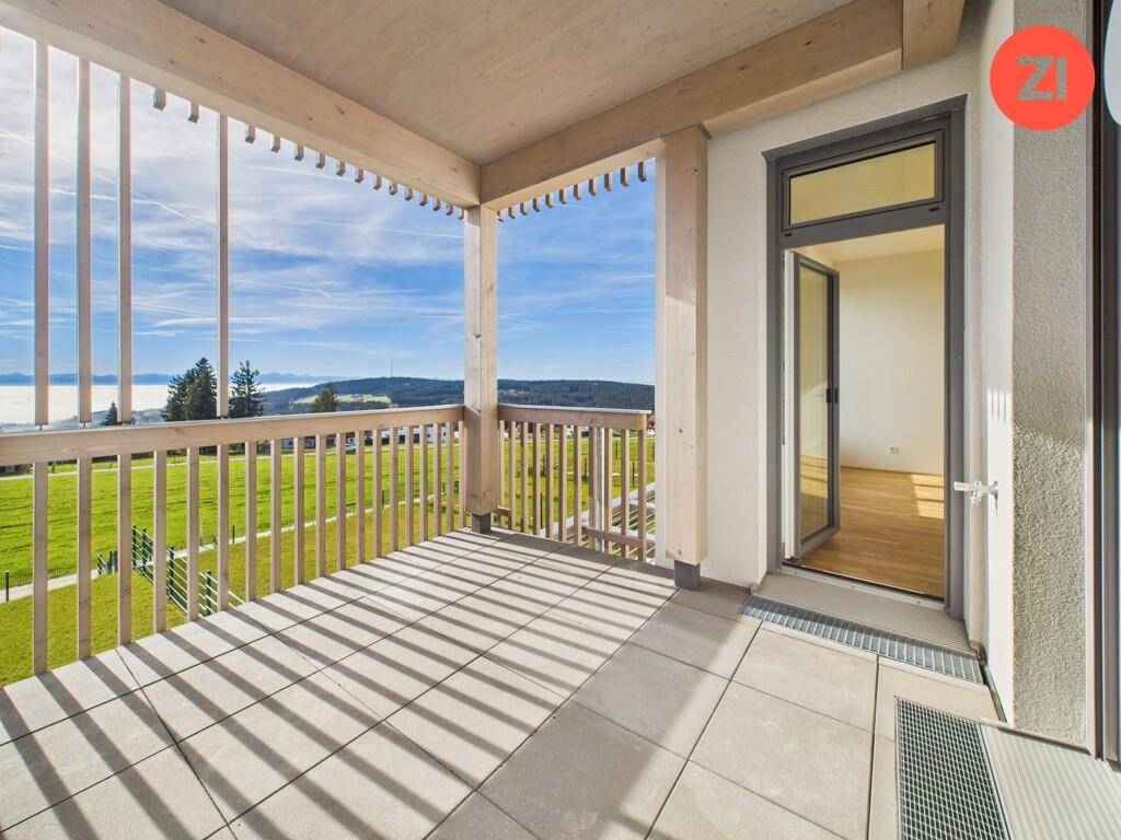 Großer Balkon mit Holzelementen, Fliesenboden und weitem Blick über grüne Hügel und Nebel.