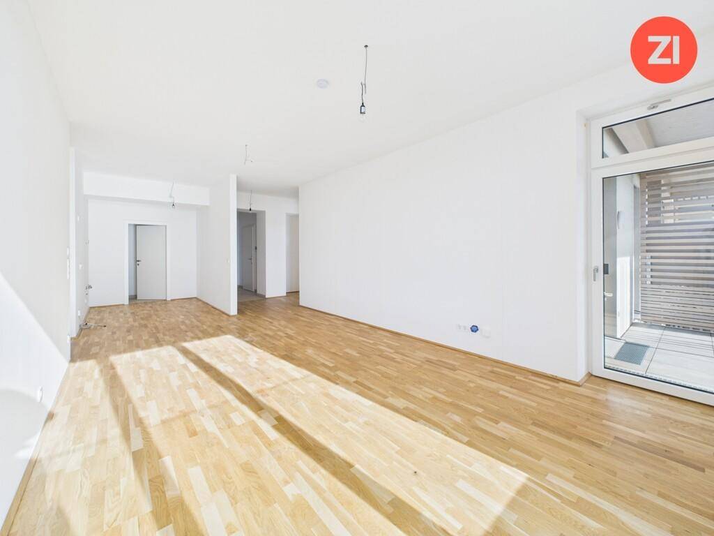 Geräumiges, leeres Wohnzimmer mit Holzboden und Zugang zu einem Balkon oder einer Terrasse.