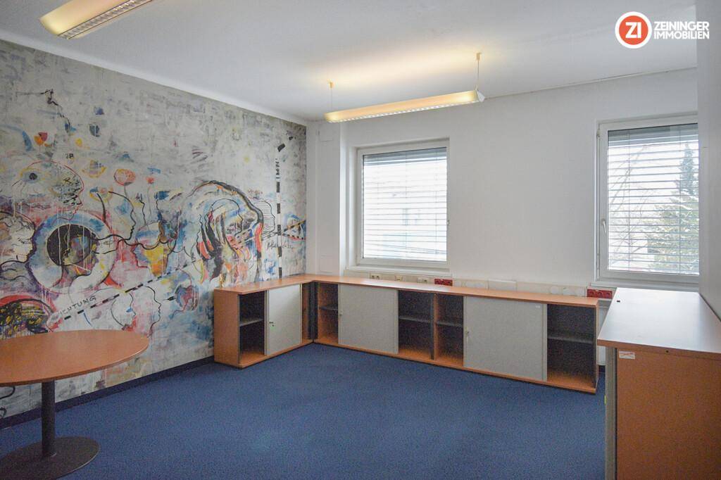 Kreativer Büroraum mit farbenfroher Wandmalerei, niedrigen Einbauschränken und Teppichboden.