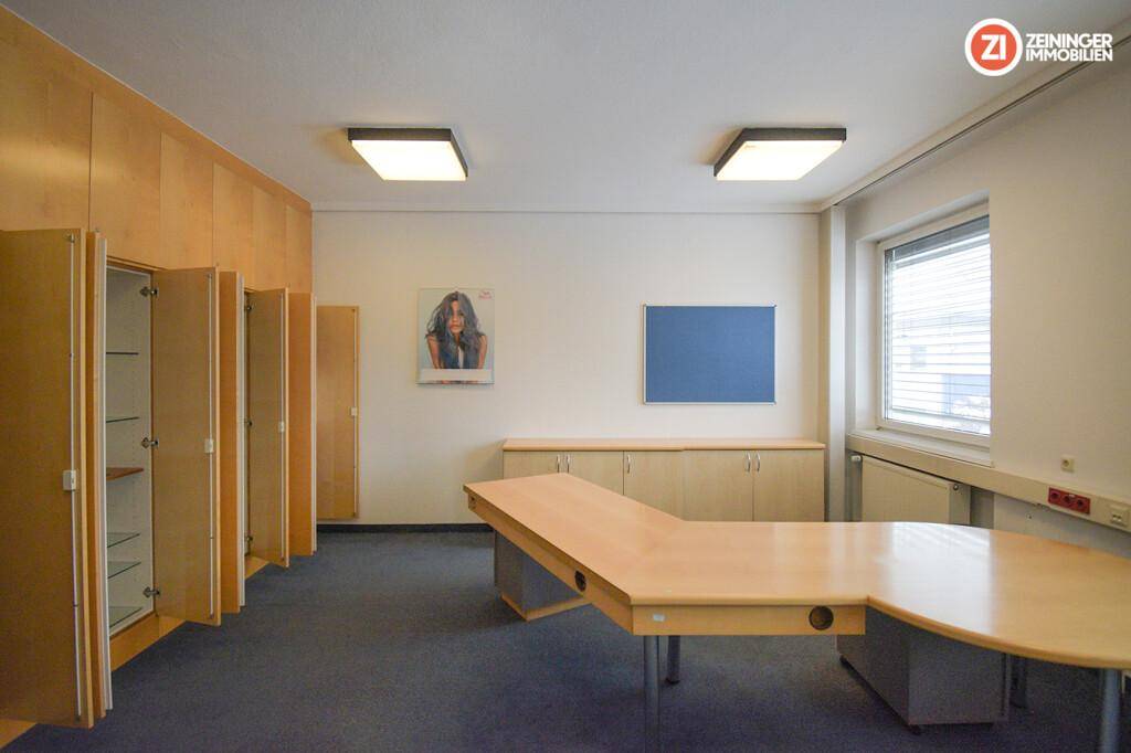Büroraum mit großem L-förmigem Schreibtisch, eingebauten Holzschränken und Teppichboden.