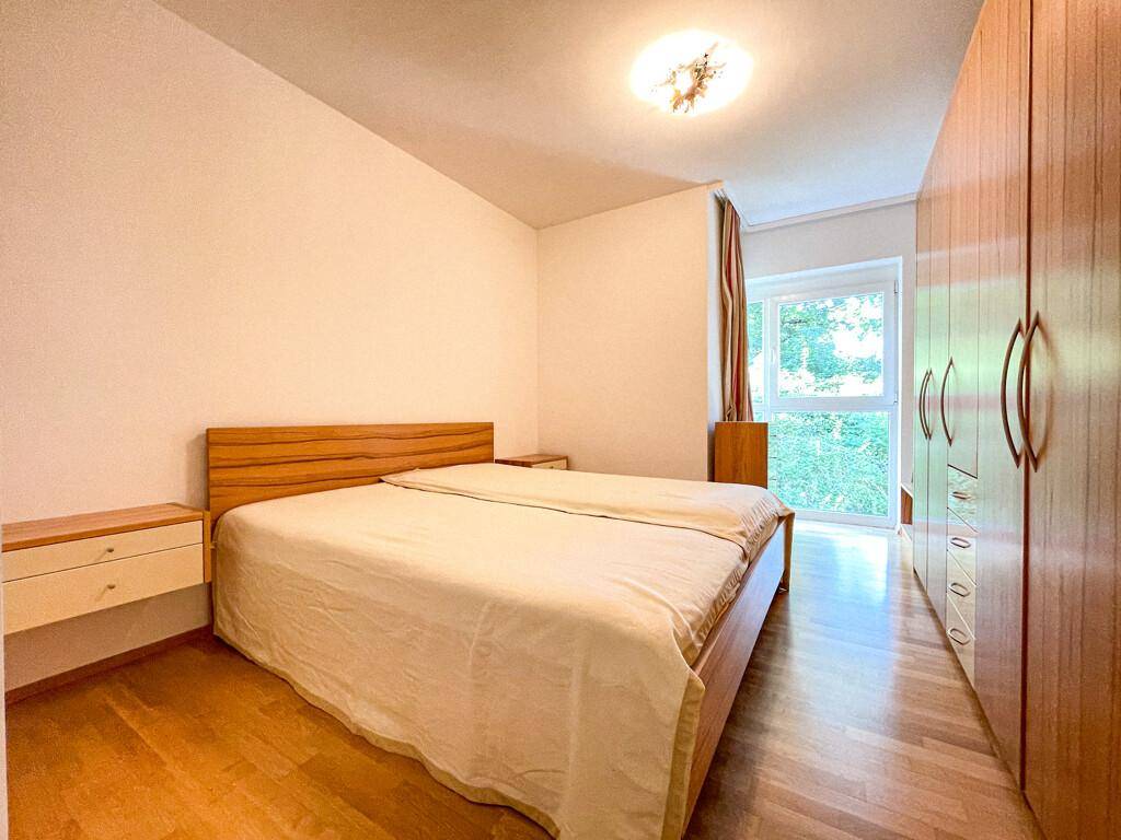 Gemütliches Schlafzimmer mit Doppelbett, Nachttischen und großem Holzschrank, mit Blick ins Grüne.