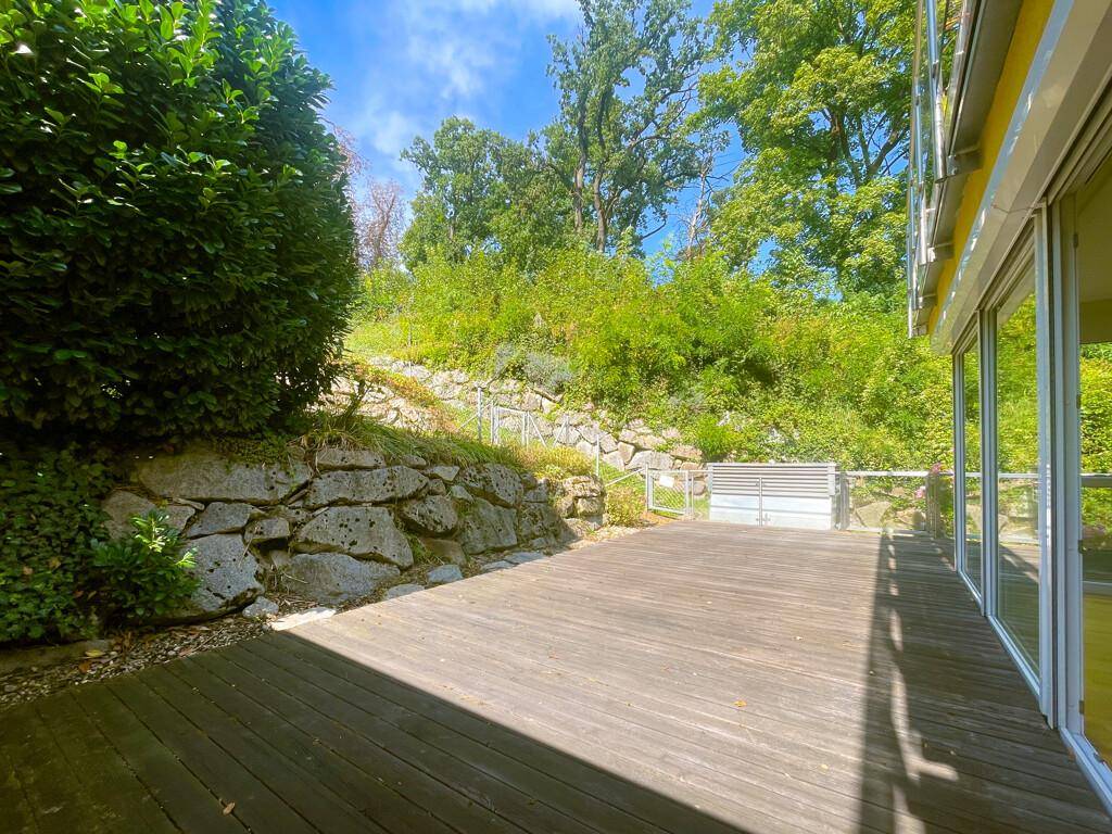 Große Holzterrasse mit Steinmauer und üppiger Bepflanzung, ideal für entspannte Stunden im Freien.