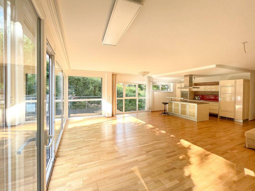 Heller, offener Wohn- und Essbereich mit integrierter Küche, Parkettboden und großen Fensterfronten zum Außenbereich.
