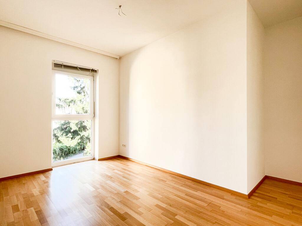 Helles Zimmer mit Parkettboden und einem großen Fenster, das einen angenehmen Blick ins Grüne bietet.