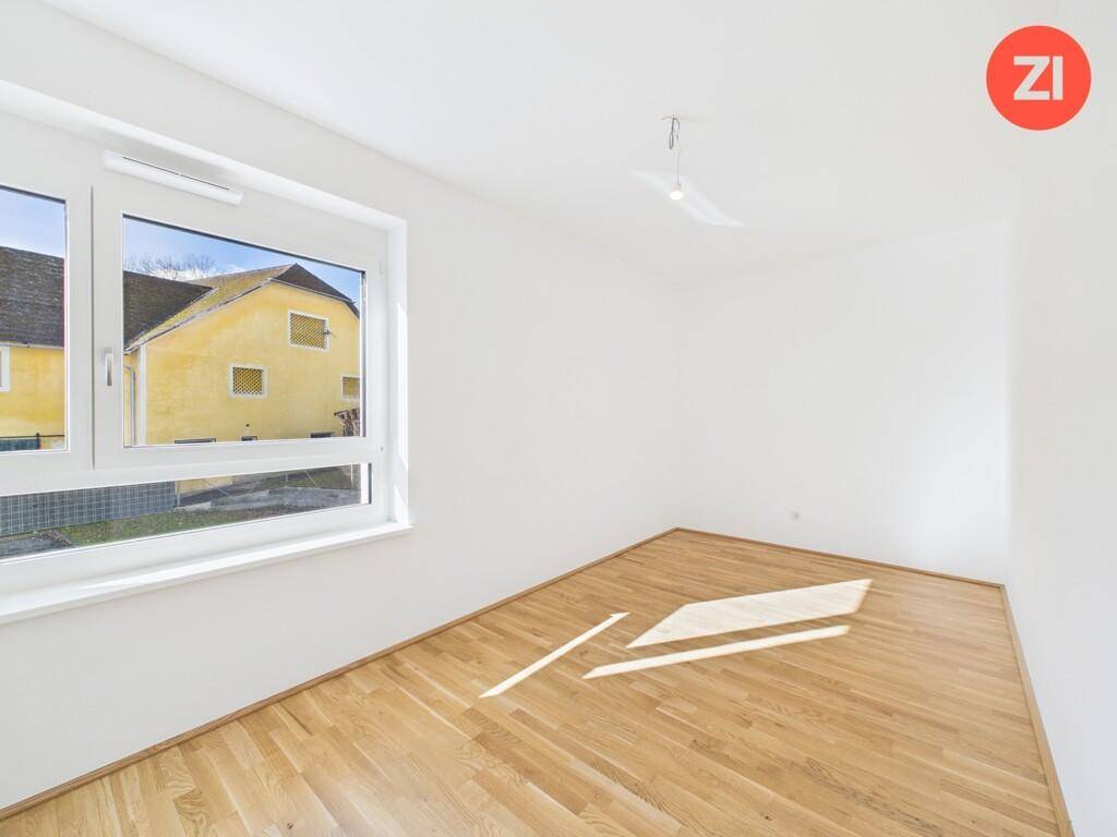 Helles Zimmer mit Parkettboden und einem großen Fenster, das viel Tageslicht hereinlässt.