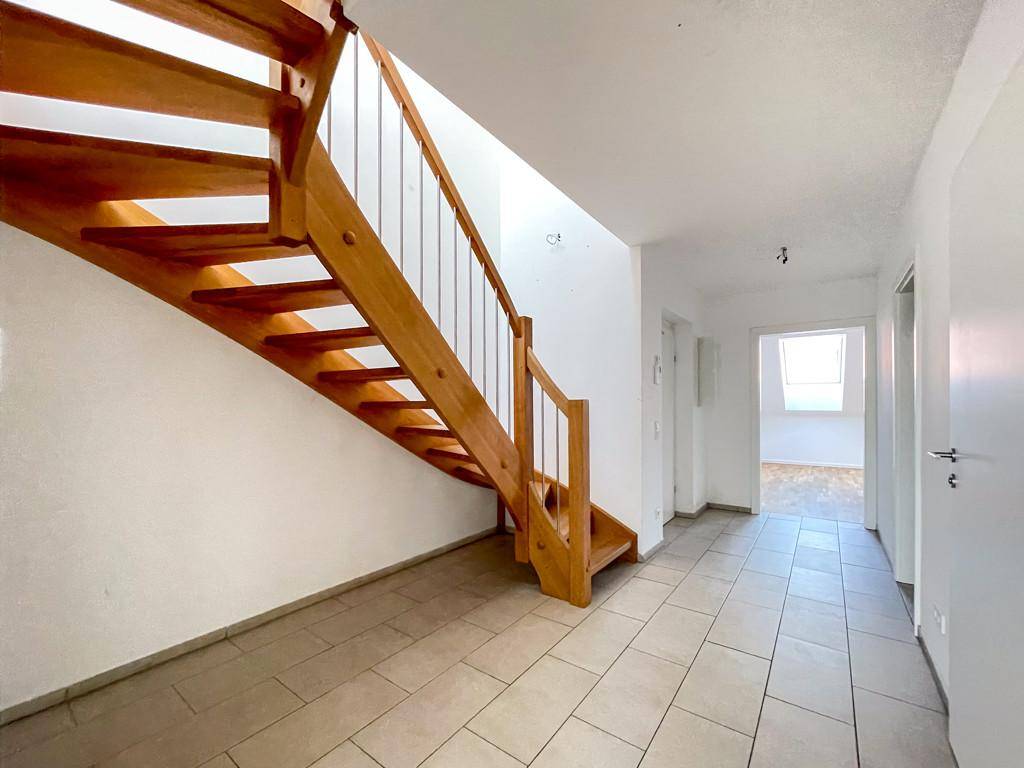 Heller Flur mit Holztreppe und Fliesenboden, der zu den oberen Räumen führt.