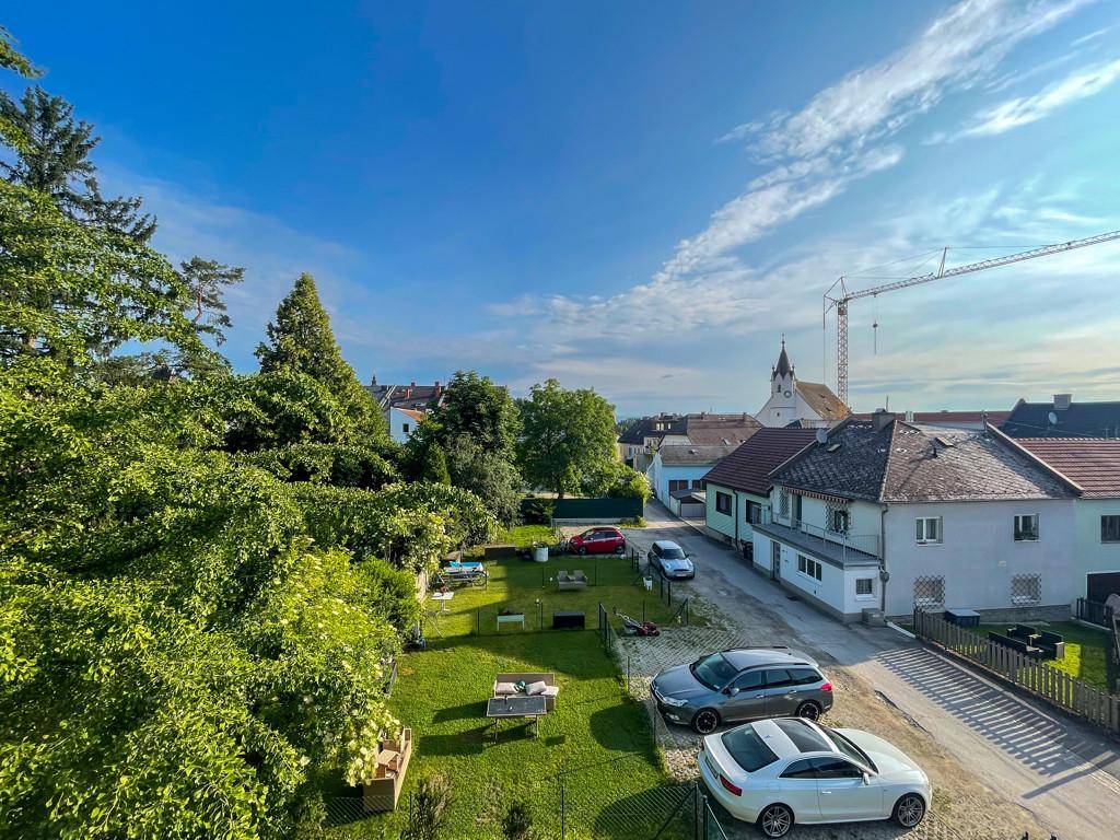 Panoramablick über eine grüne Wohngegend mit parkenden Autos und einem Kirchturm.