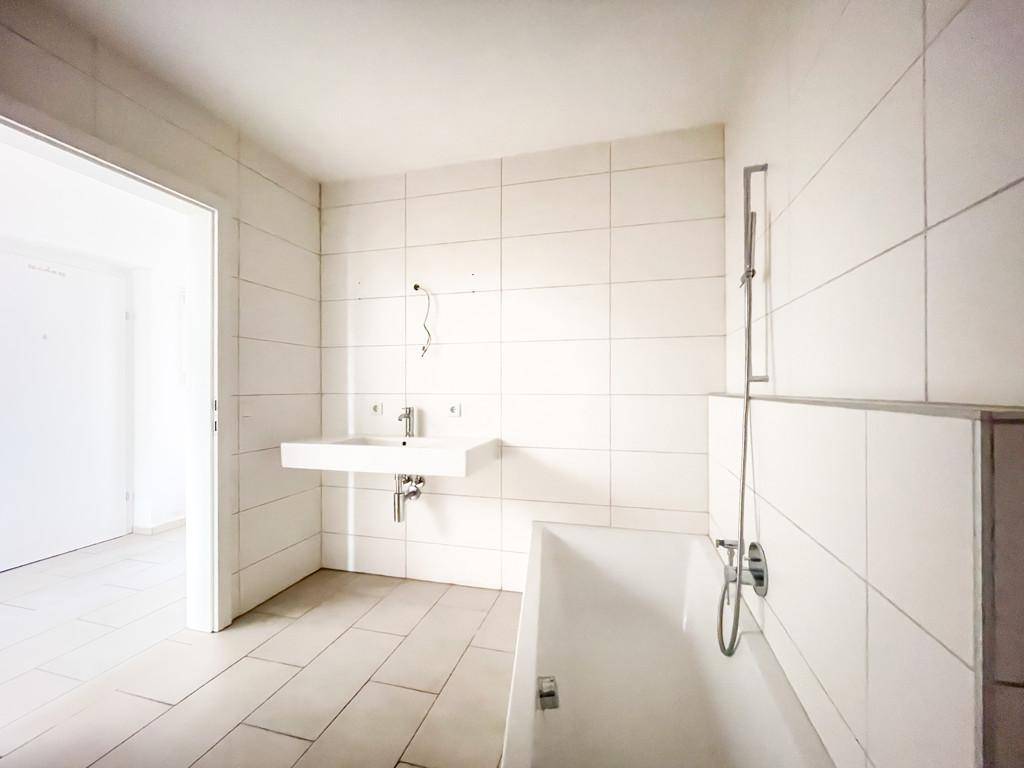 Helles Badezimmer mit Badewanne, Waschbecken und weißen Wandfliesen.