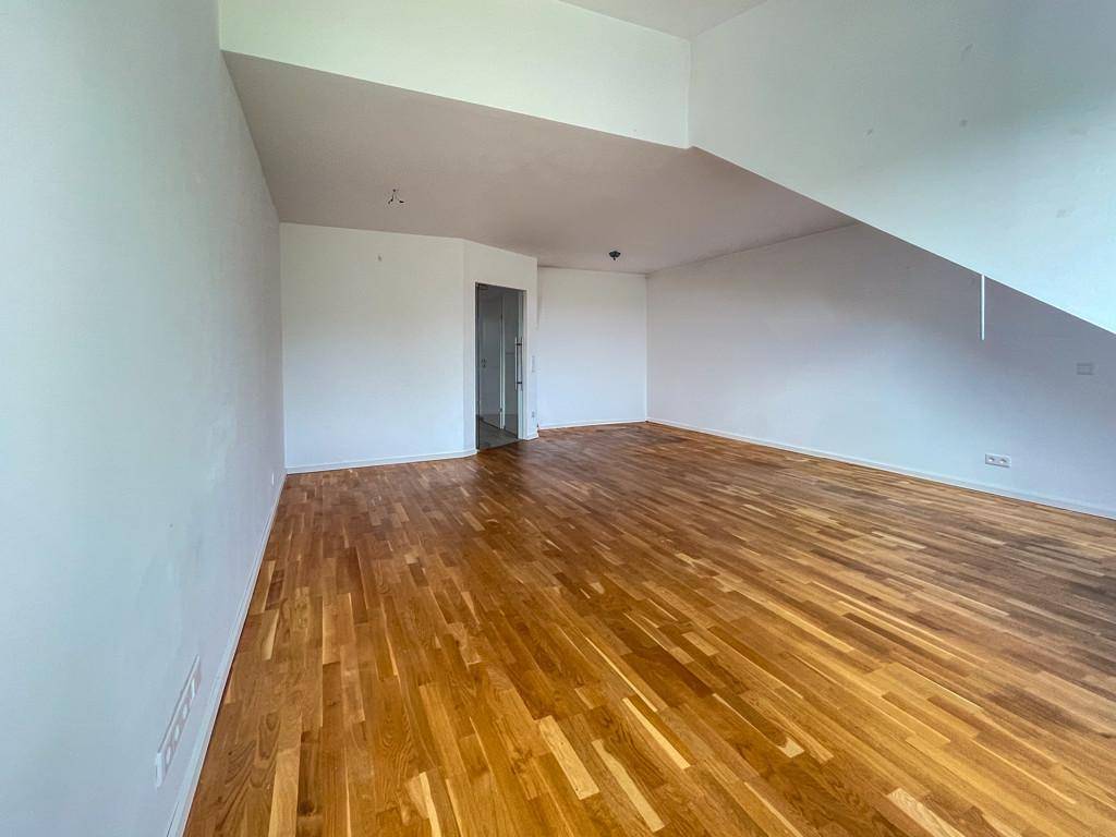 Geräumiges Wohnzimmer mit Holzboden und schrägen Wänden im Dachgeschoss.