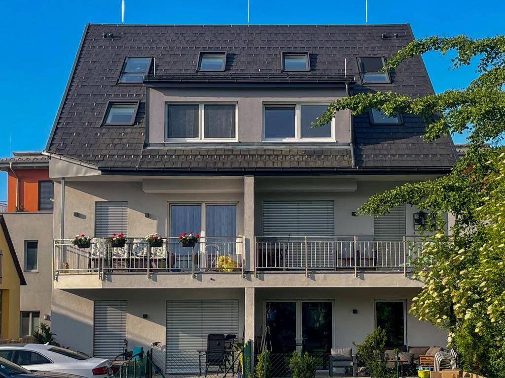 Moderne Wohnhausfassade mit mehreren Balkonen und Terrassenbereichen im Erdgeschoss.