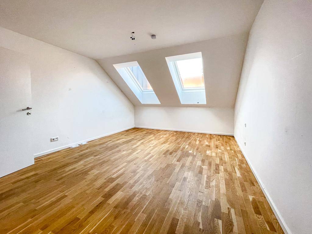 Helles Schlafzimmer im Dachgeschoss mit Holzboden und zwei Dachfenstern.