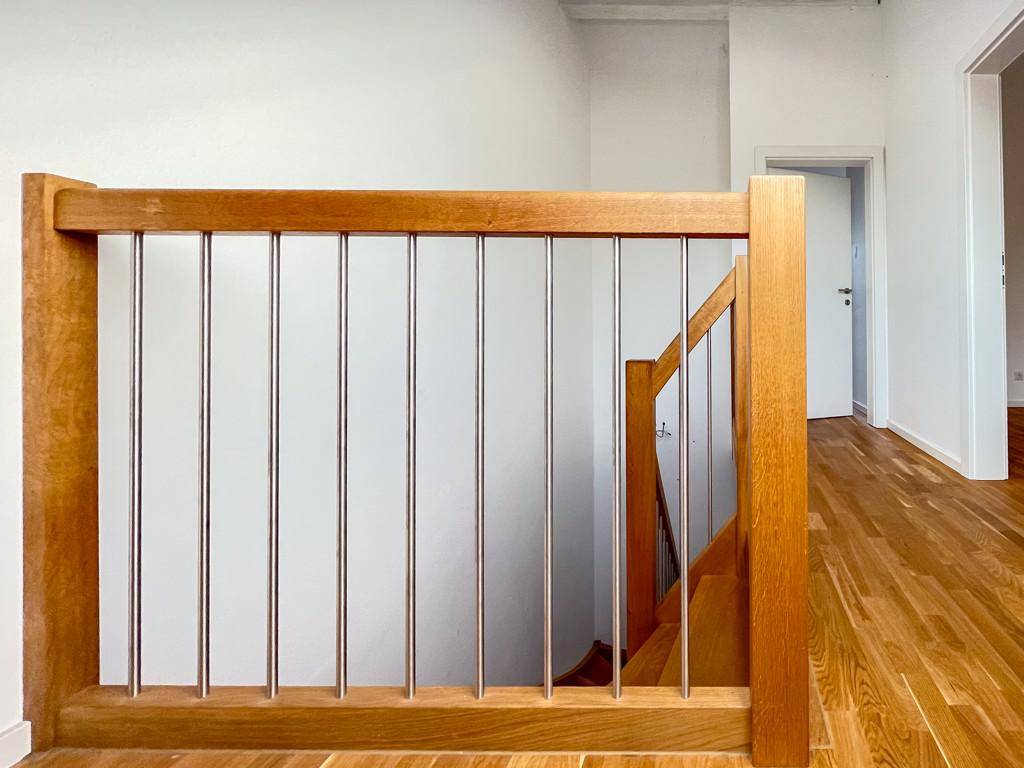 Detailansicht des Holzgeländers mit Metallstäben im Treppenhaus.