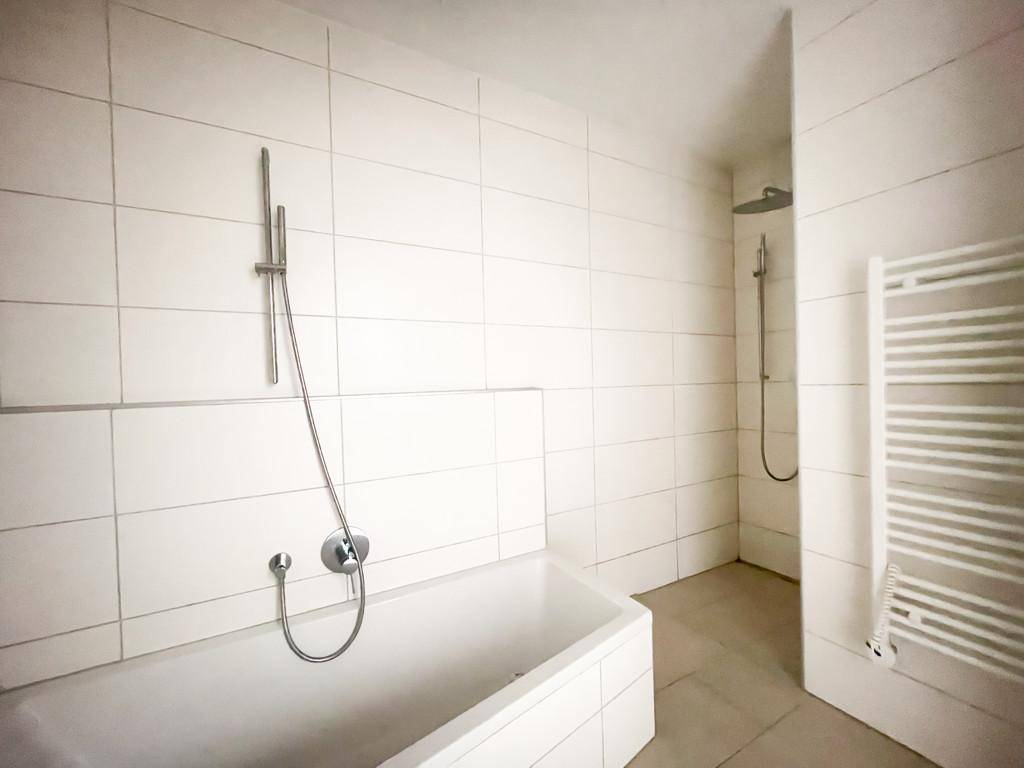 Modernes Badezimmer mit Badewanne, Dusche und weißem Fliesenboden.