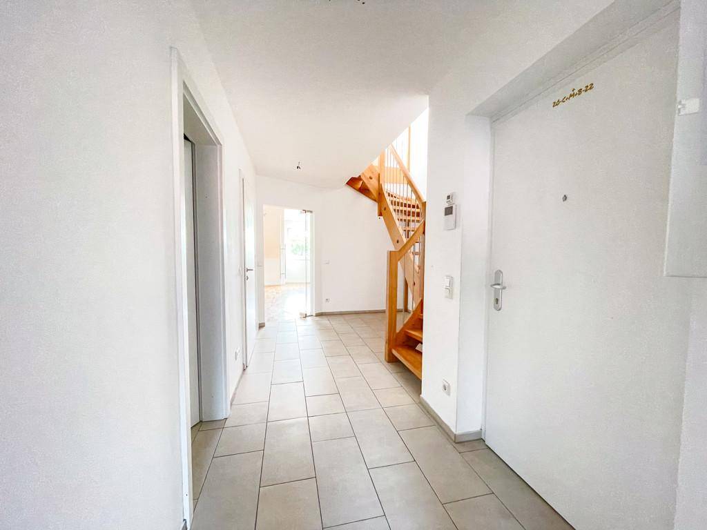 Eingangsbereich mit Fliesenboden und Holztreppe, die in die obere Etage führt.