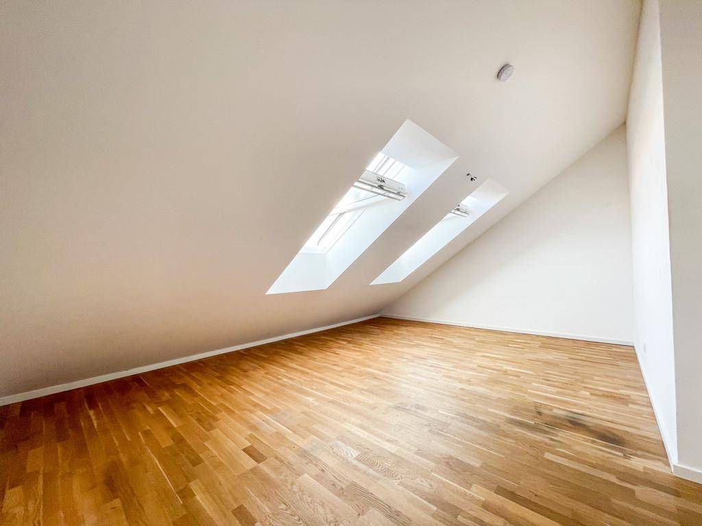 Geräumiges Dachgeschosszimmer mit Holzboden und zwei schrägen Dachfenstern.