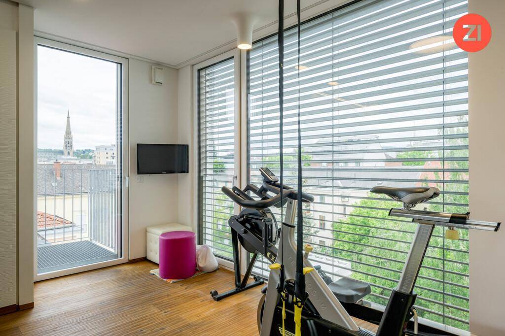 Fitnessbereich mit Trainingsgerät, Holzboden und großen Fenstern mit Stadtblick.