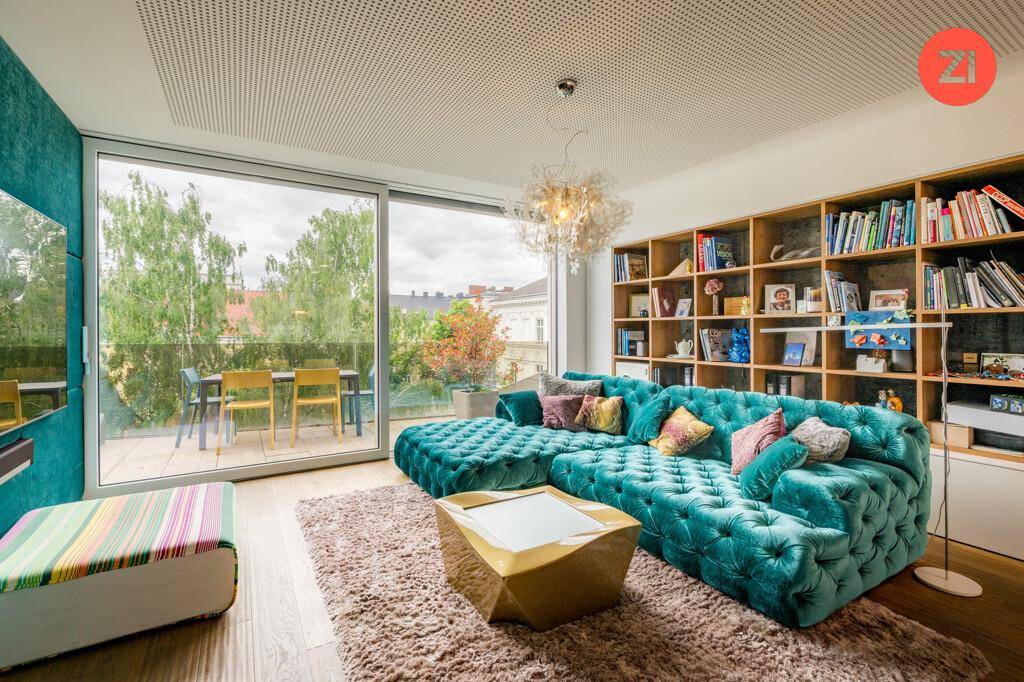 Gemütliches Wohnzimmer mit türkiser Samtcouch, Bücherregal und großen Fenstern zur Terrasse.
