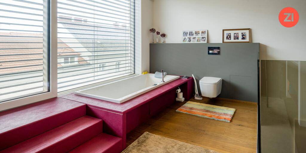 Modernes Badezimmer mit Badewanne am Fenster, Wand-WC und Holzboden.