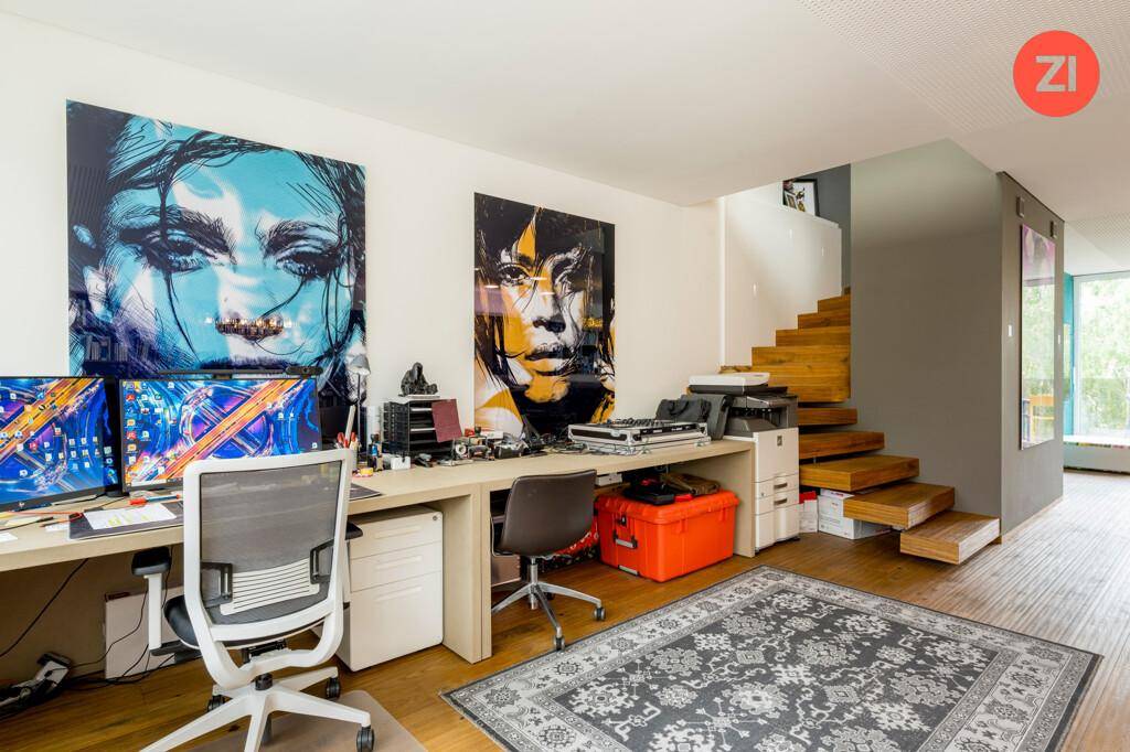Helles Arbeitszimmer mit zwei Schreibtischen, farbenfrohen Kunstwerken und Holzboden.