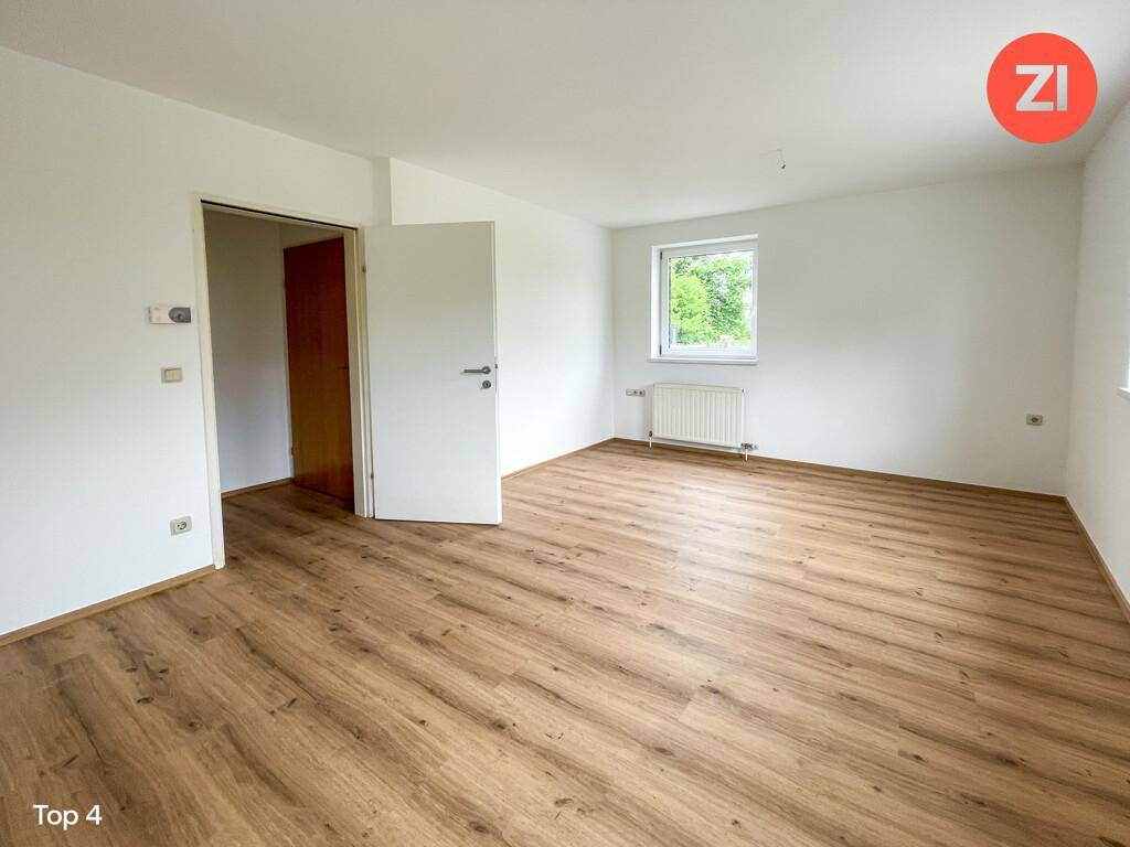 Leerer Raum, wahrscheinlich ein Wohn- oder Schlafzimmer, mit Laminatboden in Holzoptik und Fenster.