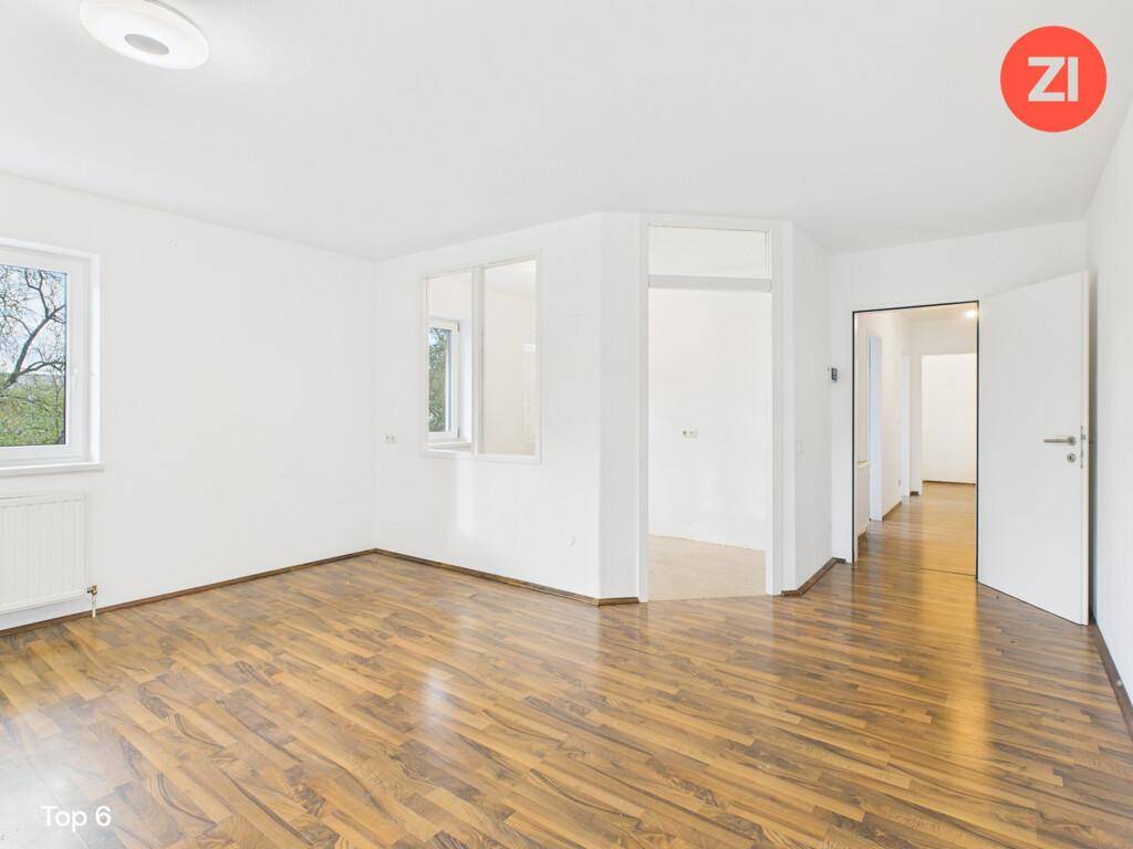 Heller, leerer Raum mit Laminatboden in Holzoptik und mehreren Fenstern für viel Tageslicht.