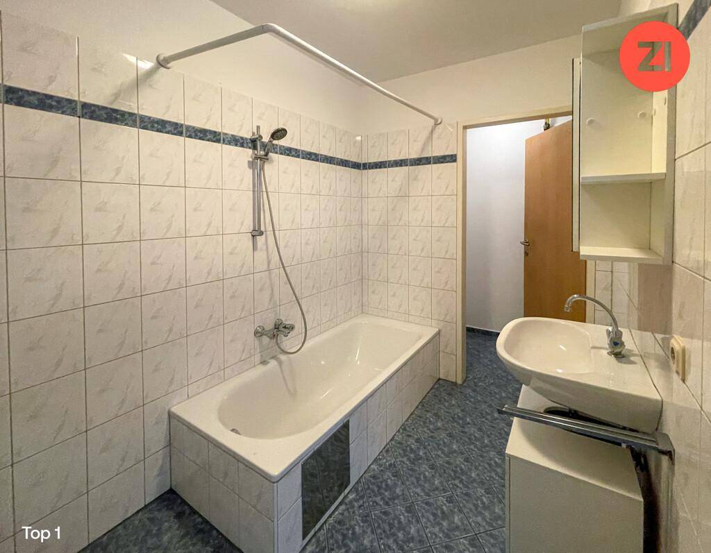Badezimmer mit weißen und blauen Fliesen, Badewanne mit Duschkopf und einem Waschbecken.