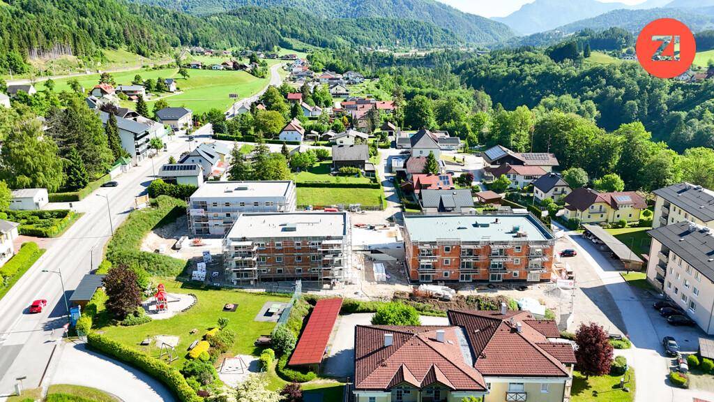Luftaufnahme einer Wohnsiedlung mit Neubauten im Bau und grüner Hügellandschaft.