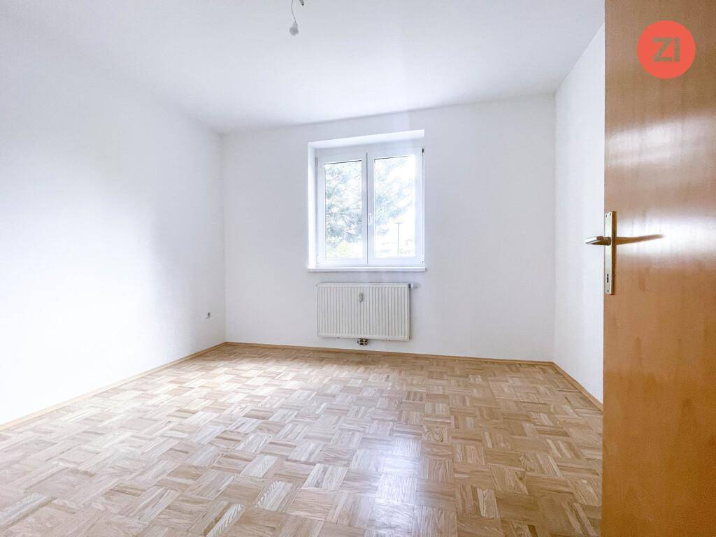 Helles Schlafzimmer mit Parkettboden und einem Fenster mit Blick ins Freie.