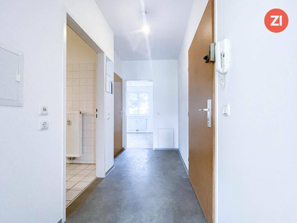 Heller Flur mit Fliesenboden und Gegensprechanlage, der zu weiteren Räumen führt.